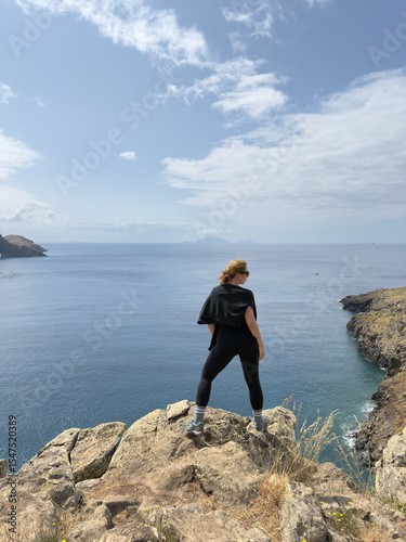 Tourist stands on edge of cliff on rocky coast of Ponta de Sao Lourenco, Madeira Island. Surrounded by waves and towering rocks, they embrace freedom and wind of environment. vertical shot.