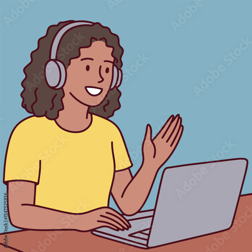 Dark skinned young woman with curly hair and headphones smiles and waves hand while having online video call or remote meeting on laptop