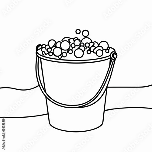 Bucket filled with foam bubbles sits on beach sand.  Bucket overflowing with soapy foam bubbles perfect for cleaning or bathing.