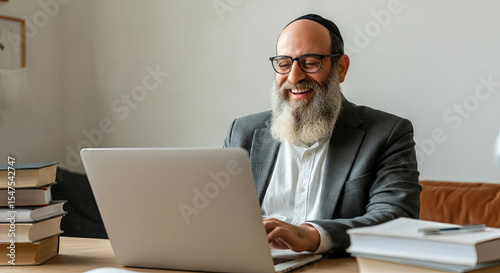 Bearded man in formal attire is working on a laptop at a wooden desk surrounded by books, showcasing a professional and focused atmosphere in a modern workspace