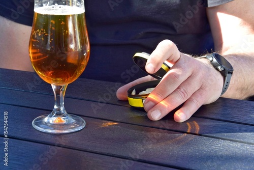 A box of snus pads in a man's hand and a glass of beer on the table.