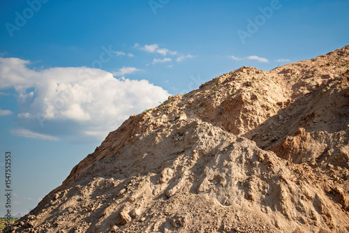 Schilderij op canvas Construction site with a large mound of soil under a bright blue sky during dayl
