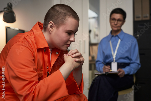 Fotografia Young Caucasian woman sitting in orange prison uniform with hands clasped, appea