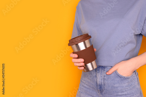 Unrecognizable woman hold in hands reusable coffee cup in front of yellow background. Take away drinks concept with copy space.