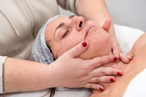 Beautician massaging face and neck of woman in beauty center