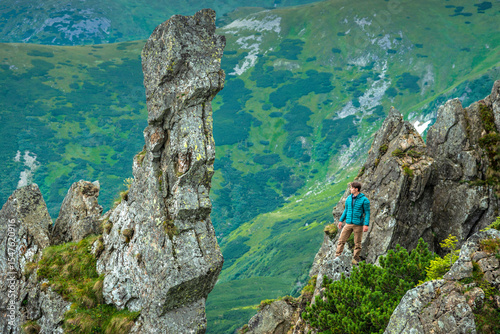 Hiker standing on rocky ridge in the Carpathian mountains, looking at scenic landscape. Alpine hiking and mountain adventure concept