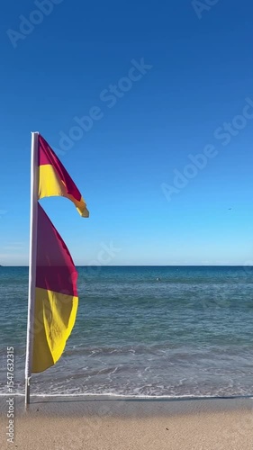 red and yellow flag on sand at the beach against clear blue sky on a sunny day in Sydney, Australia