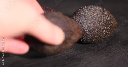 several whole black avocado fruits of small size on a black slate, ripe avocado fruit for cooking, close up