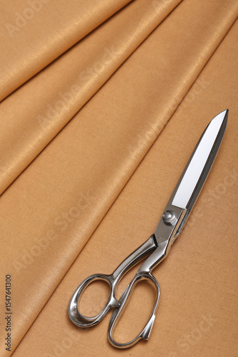 Summer fabric. Top down view of beige lightweight linen fabric with professional sewing scissors resting atop. The soft, natural texture embodies craftsmanship, tailoring and timeless textile artistry