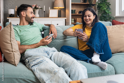 Simple living, couple goals. Young man and woman, just married sitting and hugging on sofa in their new apartment. Couple in love resting after hard day at work, enjoying in weekend activities.