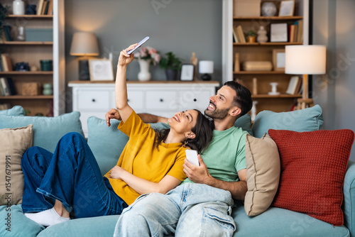 Simple living, couple goals. Young man and woman, just married sitting and hugging on sofa in their new apartment. Couple in love resting after hard day at work, enjoying in weekend activities.