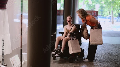 Cheerful young woman using a wheelchair and her supportive friend enjoy a shopping trip together, sharing laughter and excitement as they explore various stores