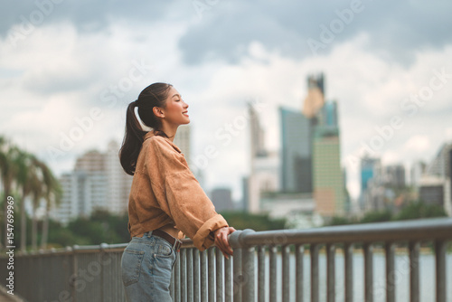 Canvastavla Cheerful asian woman standing on bridge in city park enjoying fresh air and natu