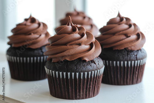 Four chocolate cupcakes with chocolate frosting on a table