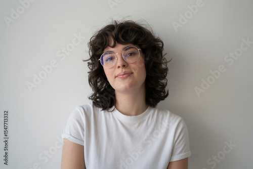 Portrait of a young woman with curly hair and glasses against white background
