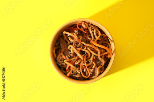 Photos Bowl of tasty Chinese noodles with vegetables and meat on yellow background