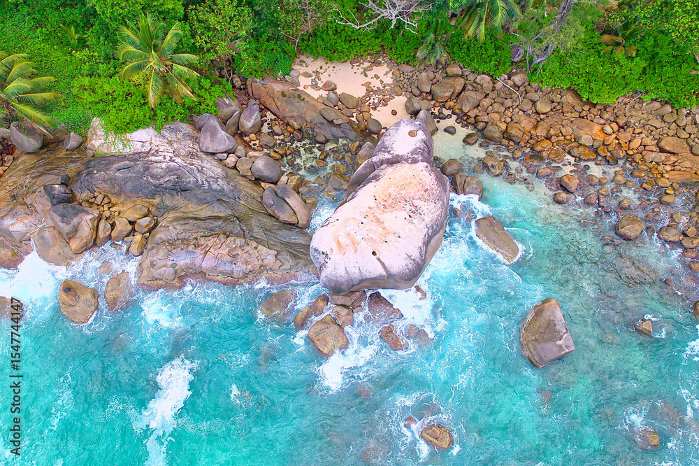 Fototapeta premium Drone shot of granite stones, wavy ocean, with pink sand, lush vegetation, Mahe Seychelles 5
