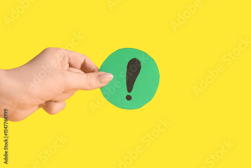 Woman holding paper exclamation mark against yellow background, closeup
