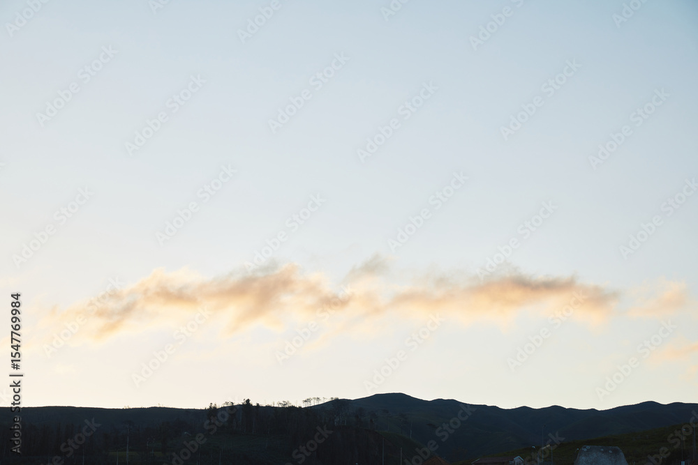 Fototapeta premium Soft cloud formation over dark hills at dawn or dusk, capturing the serene landscape with subtle light