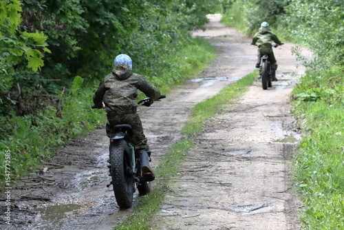 Boys in waterproof clothes and rubber boots ride fatbikes. A fat bike for off-road use