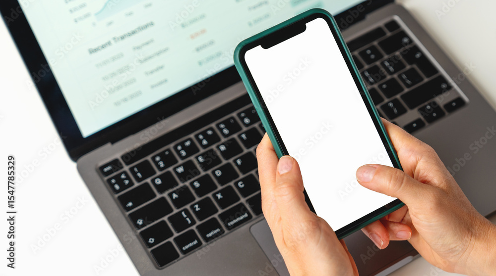 Closeup smart phone with blank screen in female hands above the laptop Closeup smart phone with blank screen in female hands above the laptop