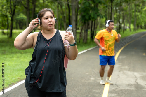 Plus size sportswoman wearing headphones  running in nature park