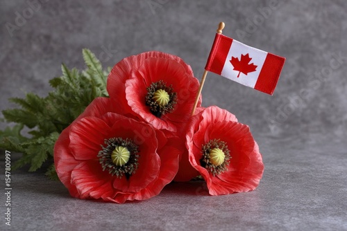 Three red poppies arranged with a small Canadian flag against a textured gray backdrop