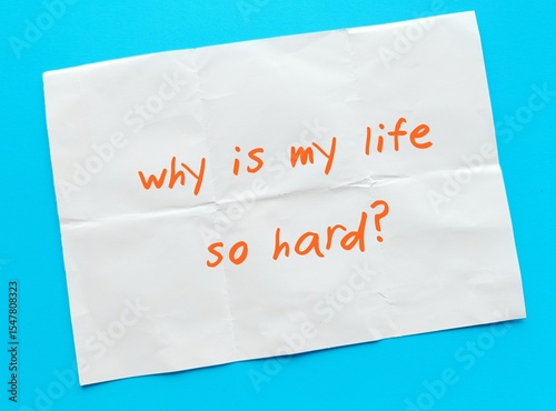 Paper on blue background with text written - Why is my life so hard? - emotional feeling with doubt when life are bad - overwhelmed with obstacles and hardship - Struggling with life challenges