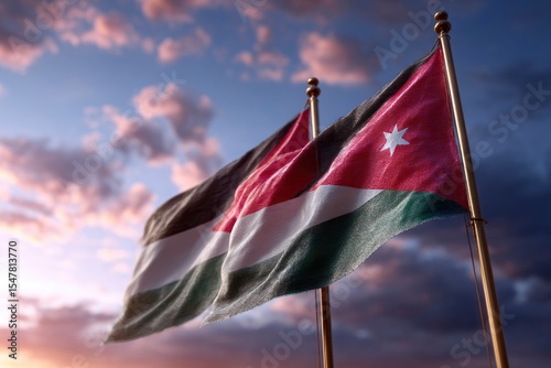 Two flags of Jordan waving against a partly cloudy twilight sky mounted on golden poles