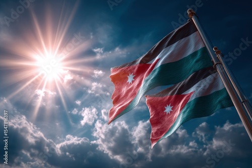 Two Jordanian flags wave in the wind against a bright sun and cloudy sky