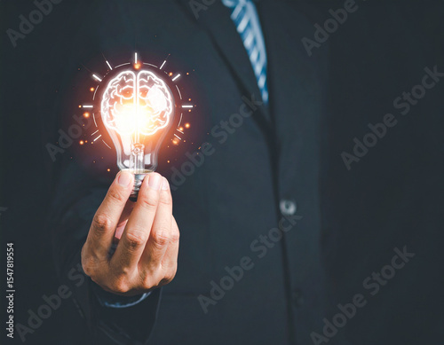 A businessman holds a lightbulb with a brain inside, symbolizing innovative thinking and creativity, illuminated against a dark backdrop.