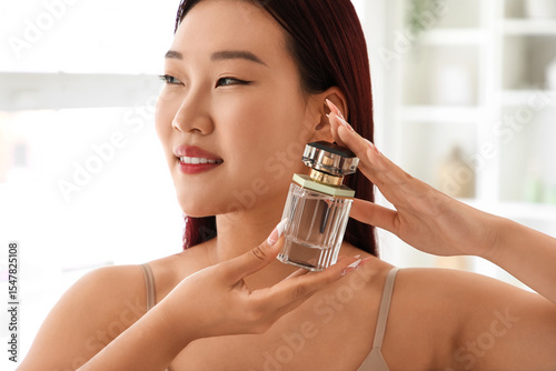 Young Asian woman with perfume in bathroom, closeup
