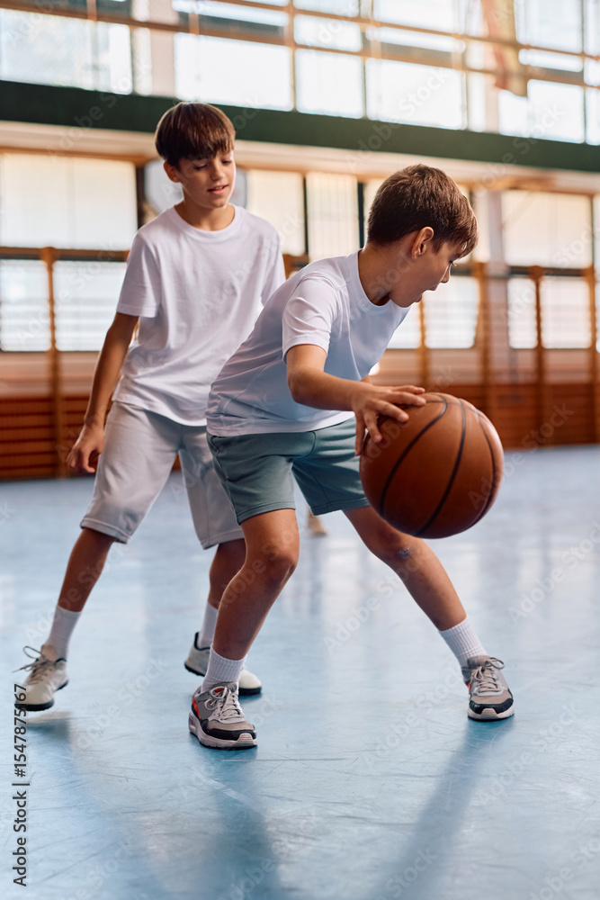 Naklejka premium Elementary students playing basketball at school gym.