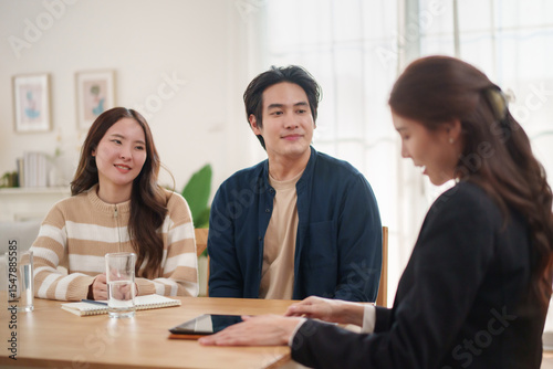 Young Asian couple attentively listening to professional female consultant during meeting at home.