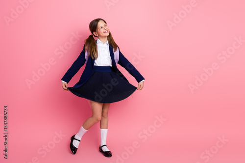 Cheerful schoolgirl posing in a neat uniform on pink background, carrying backpack, emphasizing education, confidence photo