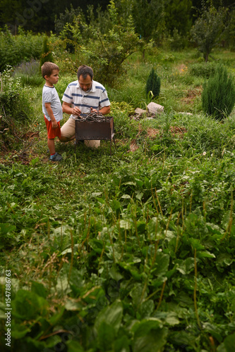 father and son light a fire for barbecue, collect brushwood and put it in the grill in the summer in the garden outdoors