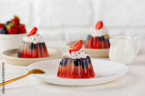 Jelly with fresh strawberry, blueberries and coconut cream on light table. Healthy food, vegan, sugar, gelatin and lactose free.