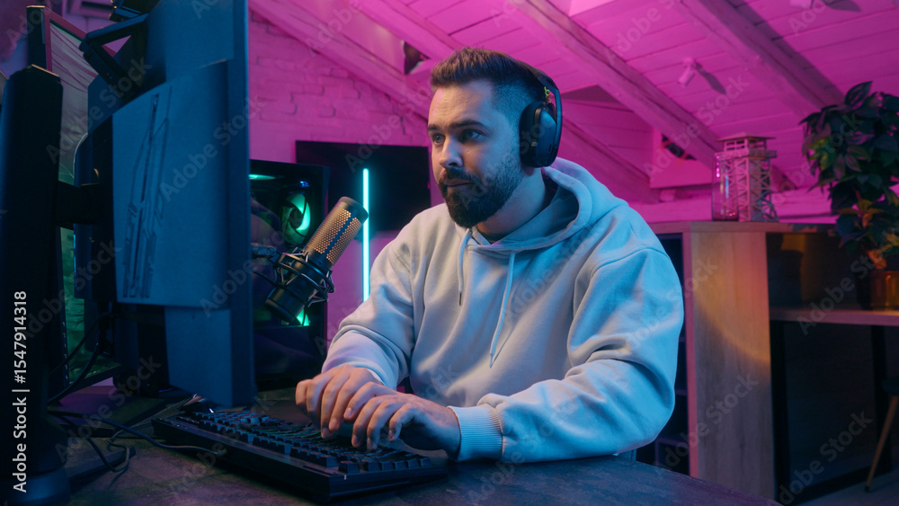 Fototapeta premium Concentrated guy male gamer streamer man wearing headphones gaming at computer focused streaming in neon light room indoors online match modern digital entertainment tech internet game playing addict