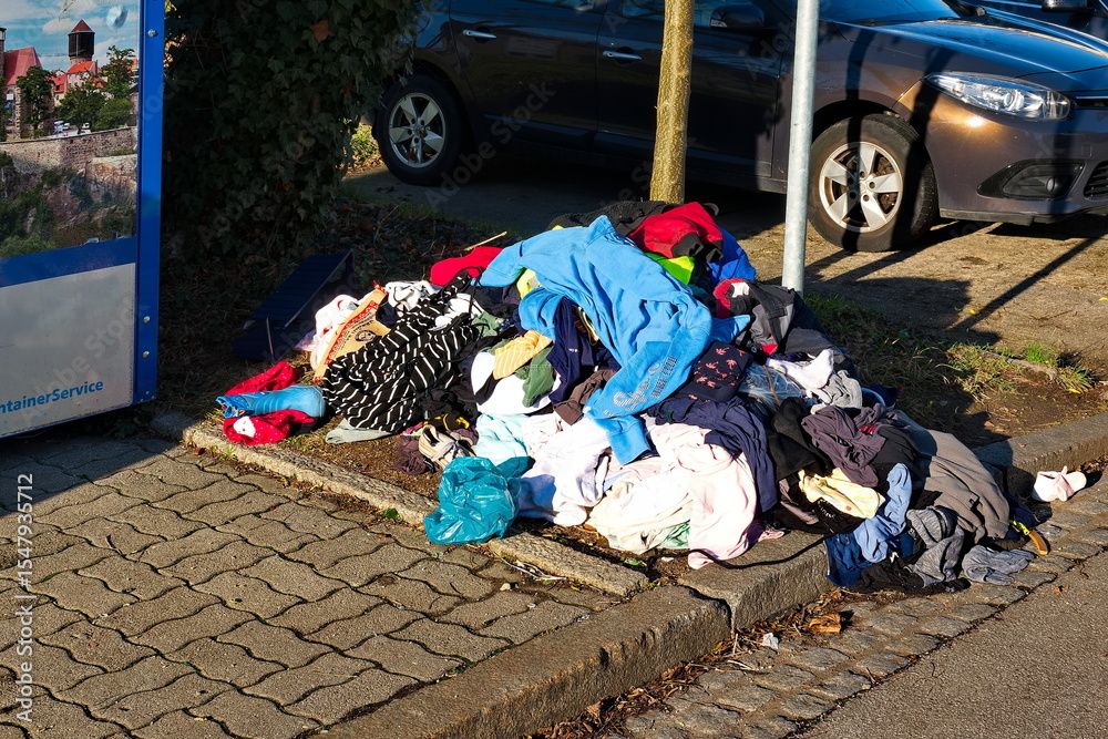 Obraz premium Wahllos Weggeworfene Altkleider neben einen Altkleidercontainer