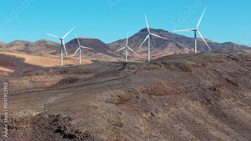 The image features wind turbines prominently situated in a breathtaking desert mountain landscape