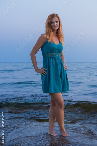 Beauty young woman walking on sea coast in blue dress. Cyprus island, blue hour