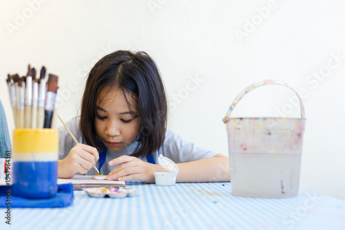 Young Asian girl focuses on painting a clay object, with her hand and brush with selective focus shows creativity and calm concentration for kid learning activity  via art and development in child.