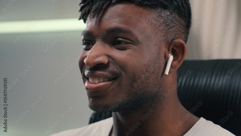 Obraz premium Close up happy smiling African American guy man ethnic male putting wireless headphones in ears listening music enjoying audio song in earphones positive relax in futuristic white studio futurism