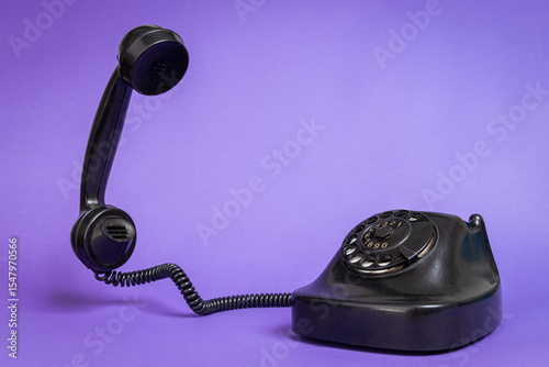 Vintage Black Rotary Dial Telephone with Handset Off the Hook on Purple Background. Retro Communication Concept for Nostalgia, History and Old Tech