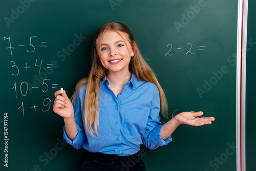 Smiling schoolgirl in blue shirt solving math problems on classroom chalkboard promoting education and learning concepts.
