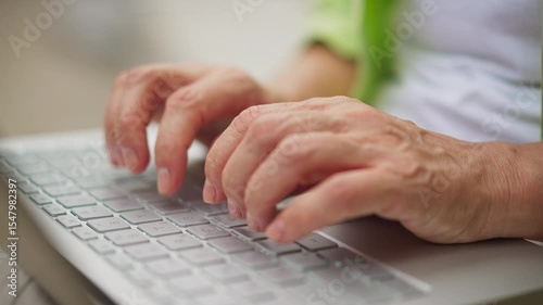 Close-up of mature hands typing on laptop keyboard. Fingers pressing keys in focused motion, working on digital tasks. Texting online. Detail. Working atmosphere. Technology concept.