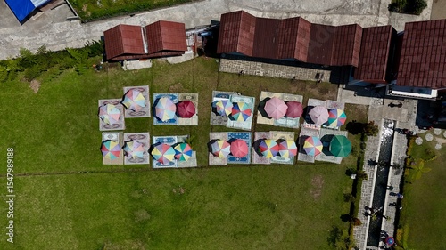 Vibrant top-down aerial view of colorful picnic setups with umbrellas and carpets on a manicured green lawn for outdoor leisure
