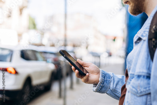 Man waiting at public transport stop using smartphone during daytime, copy space.