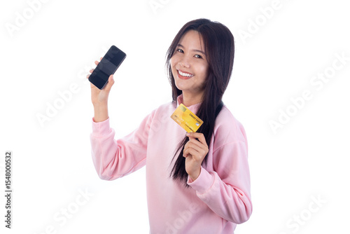 Happy Asian woman in pink sweater holding smartphone and credit card, smiling confidently on white background