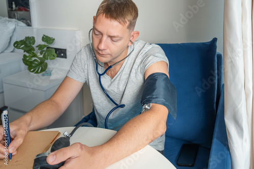 Man writing results of measuring blood pressure with manual sphygmomanometer and stethoscope at home. Hypertension measurement and tracking. Responsibility in health, routine health checks